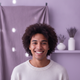 A smiling young adult in a diverse, authentic portrait headshot with a blurred background in dusty lilac and soft lavender.